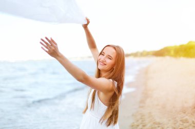 Okyanus sahilinde bulut yakalayan mutlu, mutlu, mutlu bir kadın. Beyaz yaz elbisesi içinde çok kültürlü bir kadın modelin portresi açık havada tatil sırasında doğanın tadını çıkarıyor..