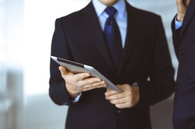 İş adamları yeni projelerini tartışmak için bir tablet bilgisayar kullanıyorlar, modern bir ofiste duruyorlar. İş yerinde iş arkadaşı olan tanınmamış bir işadamı ya da erkek girişimci.