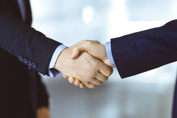 Business people shaking hands, close-up. Group of unknown businessmen standing in a modern office. Teamwork, partnership and handshake concept.
