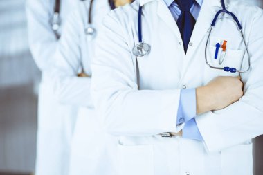 Hastane ofisinde çapraz kolları ve steteskopları olan bir grup modern doktor bir takım gibi duruyor. Doktorlar hastaları muayene etmeye ve yardım etmeye hazır. Tıbbi yardım, sağlık sigortası