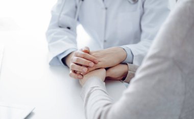 Doktor ve hasta klinikteki masada oturuyor. Kadın hekimlere odaklanıyor. Kadını rahatlatan eller. Sadece eller kapalı. Tıp konsepti.