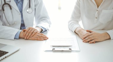 Doktor ve hasta birbirlerine yakın otururken sağlık sorularını tartışıyorlar ve klinikteki masada pano kullanıyorlar, sadece ellerini kapatıyorlar. Tıp konsepti.