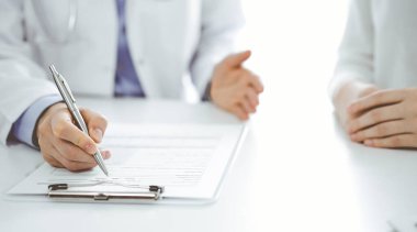 Doktor ve hasta birbirlerine yakın otururken sağlık sorularını tartışıyorlar ve klinikteki masada pano kullanıyorlar, sadece ellerini kapatıyorlar. Tıp konsepti.