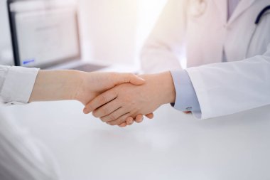 Klinikteki masada karşılıklı otururken doktor ve hasta el sıkışıyor. Sadece eller kapalı. Tıp konsepti.