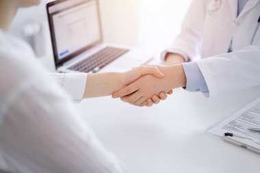 Klinikteki masada karşılıklı otururken doktor ve hasta el sıkışıyor. Sadece eller kapalı. Tıp konsepti.