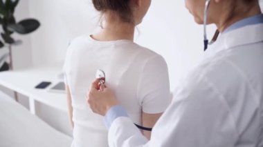 Doktor ve hasta klinikte olağan sağlık kontrolündeler. Terapist, genç bir kadını steteskopla muayene ediyor. Tıp konsepti.
