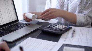 İki muhasebeci, faturalar hesaplanmayı beklerken vergi veya gelir dengesi hesaplamak için bir hesap makinesi ve dizüstü bilgisayar kullanıyor. İş denetimi ve vergi kavramları.