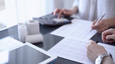 Ofisteki beyaz masada vergileri saymak için dizüstü bilgisayar ve hesap makinesi kullanan iki muhasebeci. İş denetimi ve finans alanında takım çalışması.