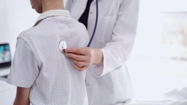 Doktor ve çocuk hasta klinikte. Beyaz önlüklü bir doktor steteskopla genç bir çocuğu muayene ediyor. İlaç, terapi konsepti.