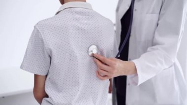 Doktor ve çocuk hasta klinikte. Beyaz önlüklü bir doktor steteskopla genç bir çocuğu muayene ediyor. İlaç, terapi konsepti.