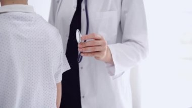 Doktor ve çocuk hasta klinikte. Beyaz önlüklü bir doktor steteskopla genç bir çocuğu muayene ediyor. İlaç, terapi konsepti.