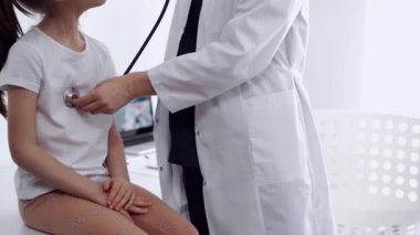 Doktor ve çocuk hasta klinikte. Beyaz önlüklü bir doktor steteskoplu genç bir kızı muayene ediyor. İlaç, terapi konsepti.