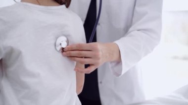 Doktor ve çocuk hasta klinikte. Beyaz önlüklü bir doktor steteskopla genç bir kızı muayene ediyor. İlaç, terapi konsepti.