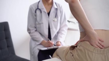 Doktor ve hasta klinikte. Beyaz önlüklü ortopedik bir kadın sırtını ovalarken not almak için pano kullanıyor, kapat. Tıp, fizik tedavi konsepti.