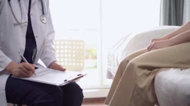 Doktor ve hasta klinikte karşı karşıya oturuyorlar, yakın çekim. Bilinmeyen kadın doktor tıbbi form doldurmak için pano kullanıyor. Tıp konsepti.