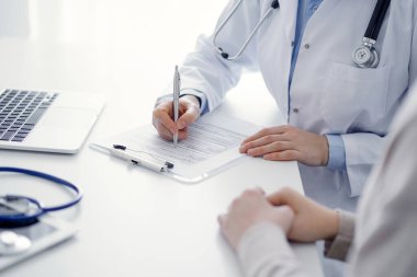 Doktor ve hasta klinikteki masada oturuyor. Kadın doktorların ellerinin tıbbi geçmiş kayıtlarını doldurması ya da kontrol listesi üzerinde yoğunlaşacağız. Kapat. Tıp konsepti.