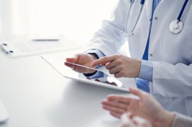 Doktor ve hasta klinikteki masada oturuyor. Tablet bilgisayar kullanan kadın doktorların ellerine odaklan, kapat. Tıp ve sağlık hizmetleri kavramı.