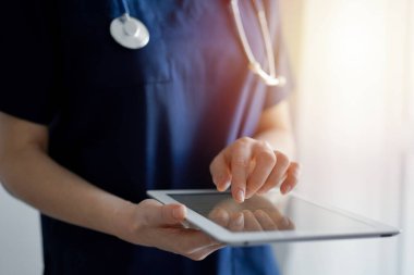 Doktor kadın panorama penceresinin yanında dururken tablet bilgisayar kullanıyor, kapatın. Doktor ya da cerrah iş başında. Tıp konsepti.