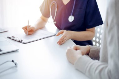 Doktor ve hasta klinikteki masada oturmuş bir şey tartışıyorlar. Kadın doktorların ellerine odaklan, yakın çekim. Tıp konsepti.