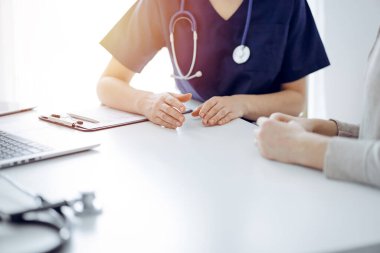 Doktor ve hasta klinikteki masada oturmuş bir şey tartışıyorlar. Kadın doktorların ellerine odaklan, yakın çekim. Tıp konsepti.