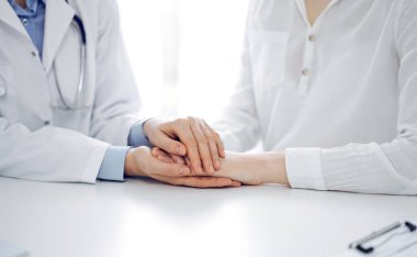 Doktor ve hasta klinikteki masada yan yana oturuyorlar. Kadın doktorlara odaklan. Kadına güven veren eller, sadece eller, yakın çekim. Tıp konsepti.