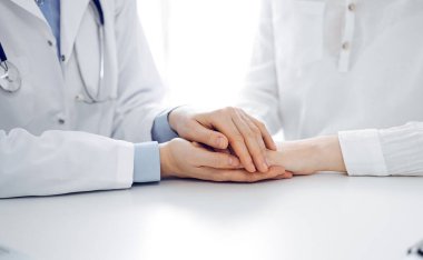 Doktor ve hasta klinikteki masada yan yana oturuyorlar. Kadın doktorlara odaklan. Kadına güven veren eller, sadece eller, yakın çekim. Tıp konsepti.