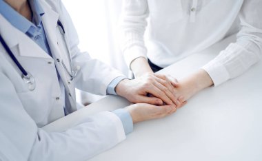 Doktor ve hasta klinikteki masada yan yana oturuyorlar. Kadın doktorlara odaklan. Kadına güven veren eller, sadece eller, yakın çekim. Tıp konsepti.