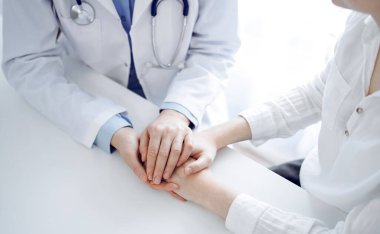 Doktor ve hasta klinikteki masada yan yana oturuyorlar. Kadın doktorlara odaklan. Kadına güven veren eller, sadece eller, yakın çekim. Tıp konsepti.