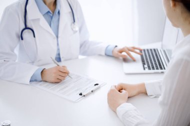 Doktor ve hasta bir şey tartışıyor ve klinikteki masada karşılıklı otururken dizüstü bilgisayar kullanıyorlar. Mükemmel tıbbi hizmet ve tıp konsepti.