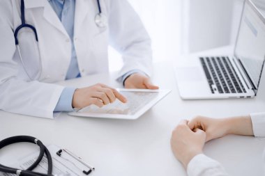 Doktor ve hasta klinikteki masada karşılıklı oturuyorlar. Tablet bilgisayar kullanan kadın doktorların ellerine odaklan, kapat. Tıp konsepti.