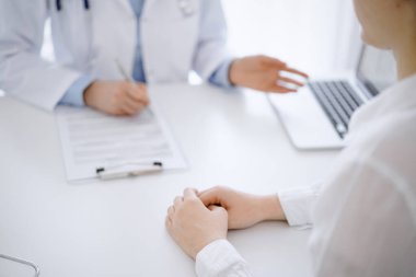 Doktor ve hasta klinikteki masada karşılıklı otururken tablet bilgisayar kullanıyorlar. Doktorun yanındaki kadın ellerine odaklan, yakın çekim. Tıp konsepti.
