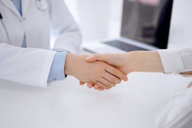 Klinikteki masada karşılıklı otururken doktor ve hasta el sıkışıyor. Sadece eller kapalı. Tıp konsepti.