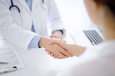 Klinikteki masada karşılıklı otururken doktor ve hasta el sıkışıyor. Sadece eller kapalı. Tıp konsepti.