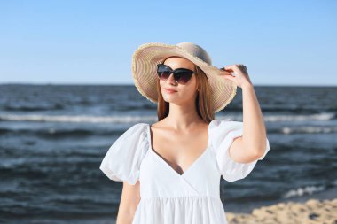 Mutlu sarışın kadın okyanus sahilinde güneş gözlüğü ve şapkasıyla poz veriyor. Akşam güneşi.