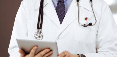 Klinikte dururken elinde tablet bilgisayar tutan kimliği belirsiz bir erkek doktor. Coronavirüs salgını sırasında ilaç kavramı.