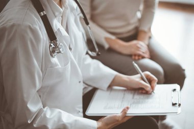 Doktor ve hasta klinikteki koltukta oturuyor. Kadın doktorların ellerinin ilaç geçmişi formunu doldurmasına odaklan, kapat. Tıp konsepti.