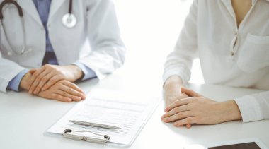 Doktor ve hasta birbirlerine yakın otururken sağlık sorularını tartışıyorlar ve klinikteki masada pano kullanıyorlar, sadece ellerini kapatıyorlar. Tıp konsepti.