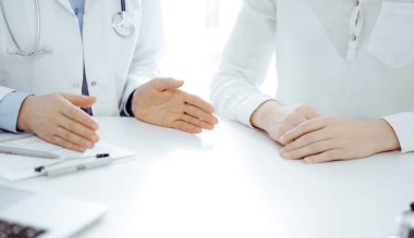 Doktor ve hasta klinikteki masada yan yana otururken sağlık sorunlarını tartışıyorlar. Sadece ellerinizi yakın tutun. Tıp konsepti.