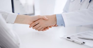 Klinikteki masada karşılıklı otururken doktor ve hasta el sıkışıyor. Sadece eller kapalı. Tıp konsepti.