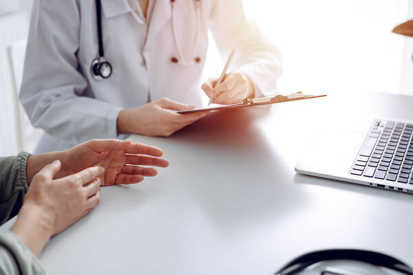 Doctor and patient discussing current health examination while sitting at the desk in clinic office, closeup. Medicine concept.
