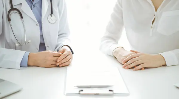 Doctor and patient discussing current health questions while sitting near of each other and using clipboard at the table in clinic, just hands closeup. Medicine concept.