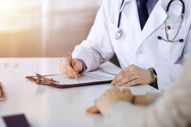 Bilinmeyen bir erkek doktor ve hasta kadın karanlık bir klinikte otururken bir şey tartışıyorlar ve arka planda pano kullanıyorlar..