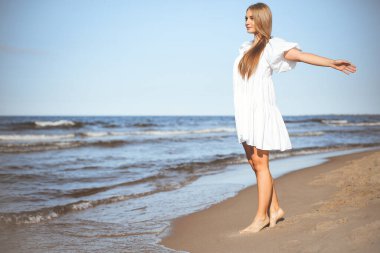Mutlu gülümseyen güzel kadın okyanus sahilinde kollarını açmış yürüyor..