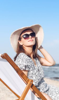 Okyanus sahilinde tahta bir iskemlede dinlenirken güneş gözlüğü takan mutlu esmer kadın..