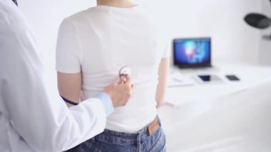 Doktor ve hasta klinikte olağan sağlık kontrolündeler. Terapist, genç bir kadını steteskopla muayene ediyor. Tıp konsepti.
