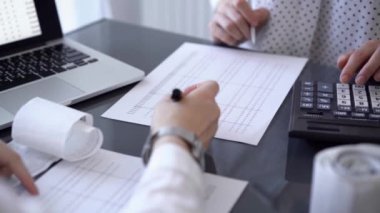 İki muhasebeci, faturalar hesaplanmayı beklerken vergi veya gelir dengesi hesaplamak için bir hesap makinesi ve dizüstü bilgisayar kullanıyor. İş denetimi ve vergi kavramları.