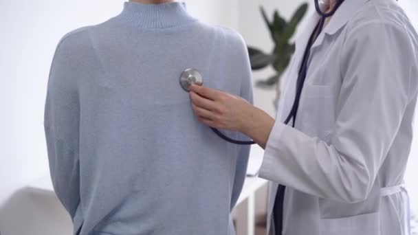 医師と患者さんは診療所にいます 白いコートを着た医師が 女性を診察して 直ぐに近づけます セラピーコンセプト — ストック動画