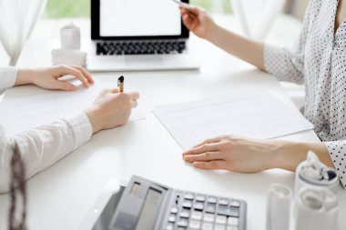 Beyaz masadaki vergileri saymak için dizüstü bilgisayar kullanan iki muhasebeci. İş kadını elinde kalemle ekranı işaret ediyor. İş denetimi ve finans alanında takım çalışması.