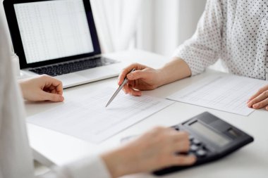 Ofisteki bir müşteriyle ya da meslektaşıyla vergi saymak için hesap makinesi ve dizüstü bilgisayar kullanan bir muhasebeci. İş denetimi ve finans alanında takım çalışması.