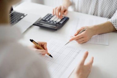 Ofisteki bir müşteriyle ya da meslektaşıyla vergi saymak için hesap makinesi ve dizüstü bilgisayar kullanan bir muhasebeci. İş denetimi ve finans alanında takım çalışması.